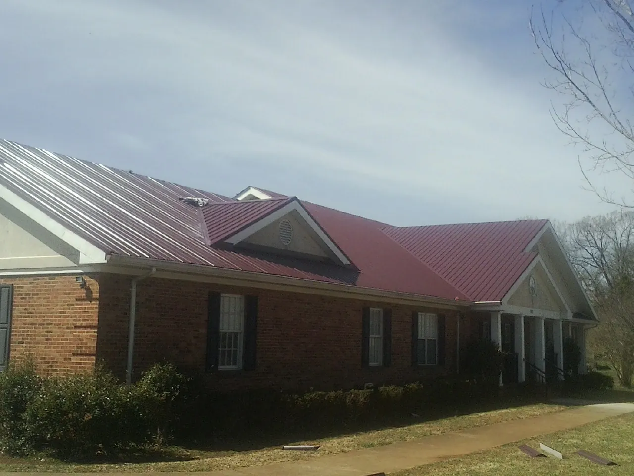 Red metal roof with gabled entries on a long brick building, from a Hail Damage Roof Repair job in Sutter Creek