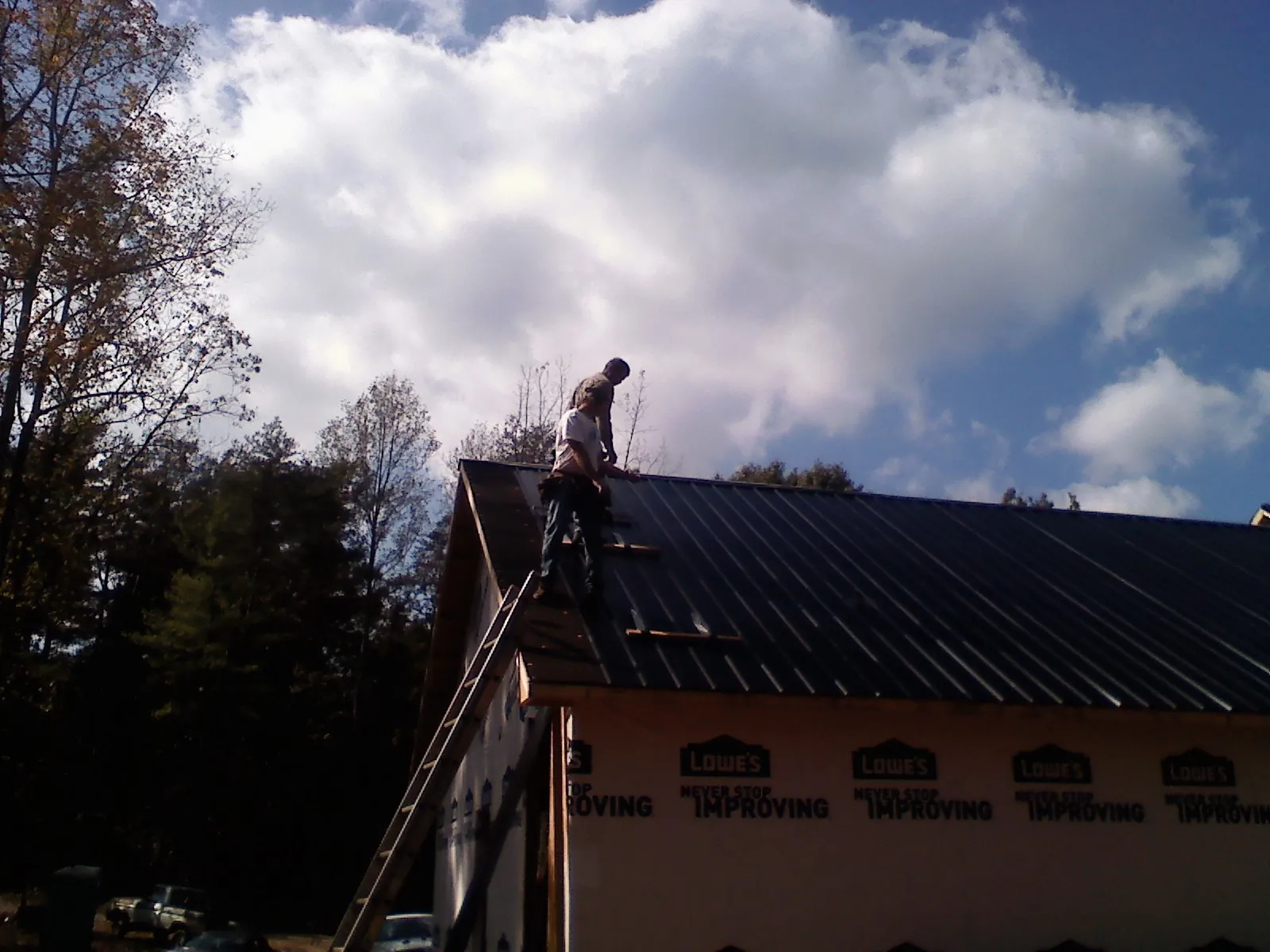 Roofer fastening dark metal panels high against a cloudy sky, from a Roof Inspection job in Sutter Creek